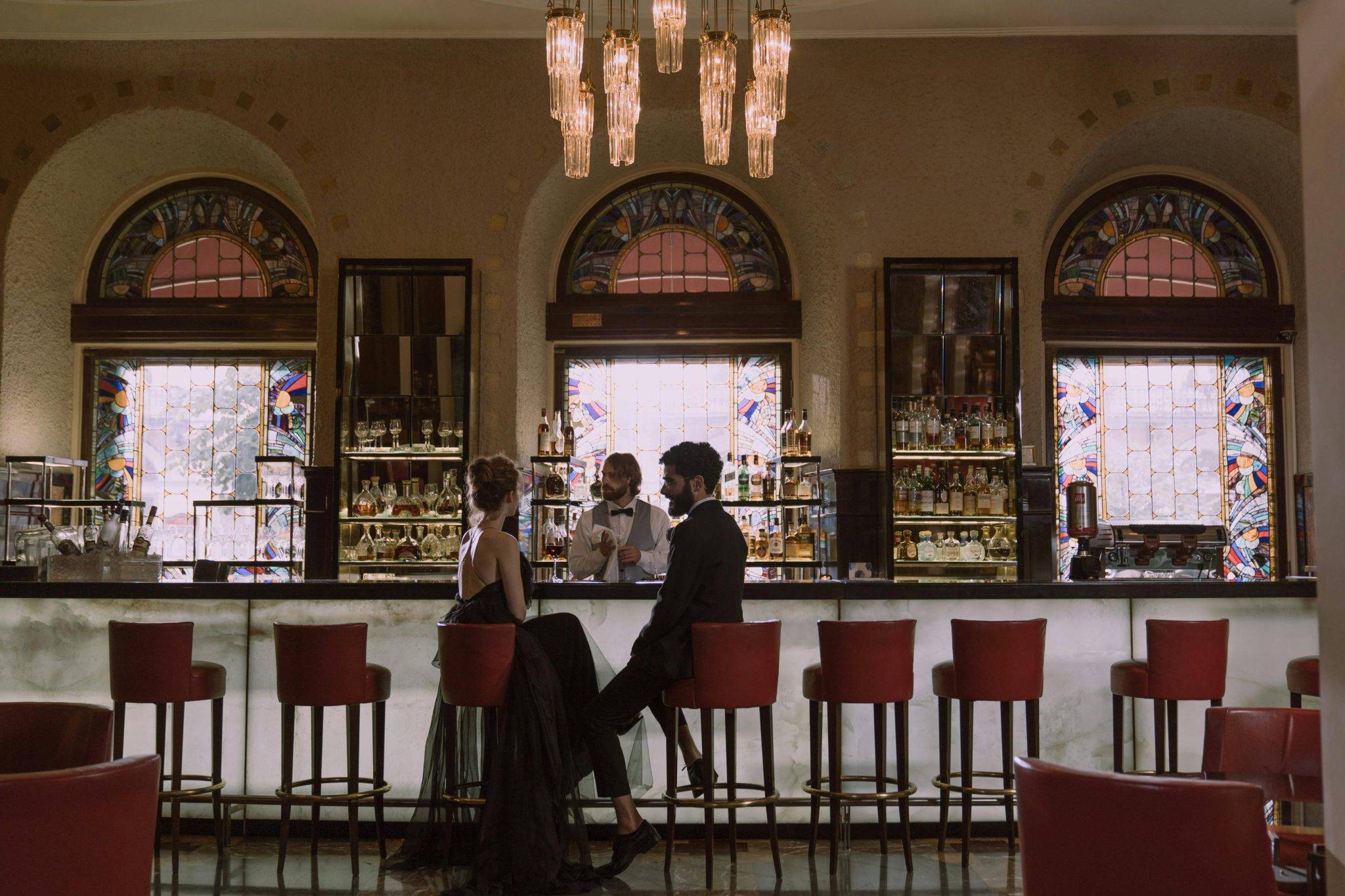 Couple in elegant attire enjoying a date at a luxurious bar with a stained glass backdrop in AI for hospitality.